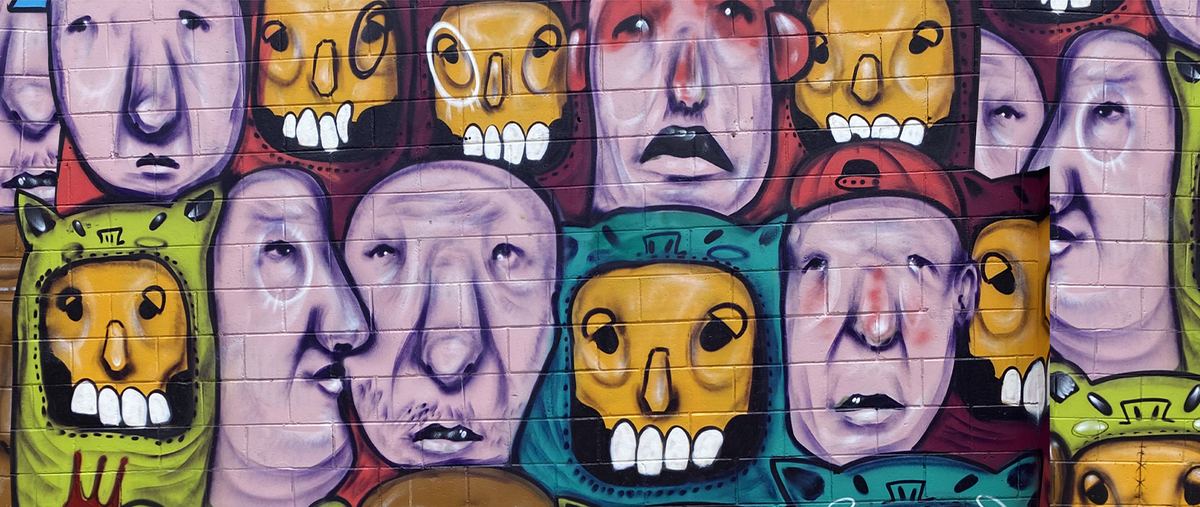 Detalhe de mural com rostos e caveiras amarelas sobre parede de tijolos