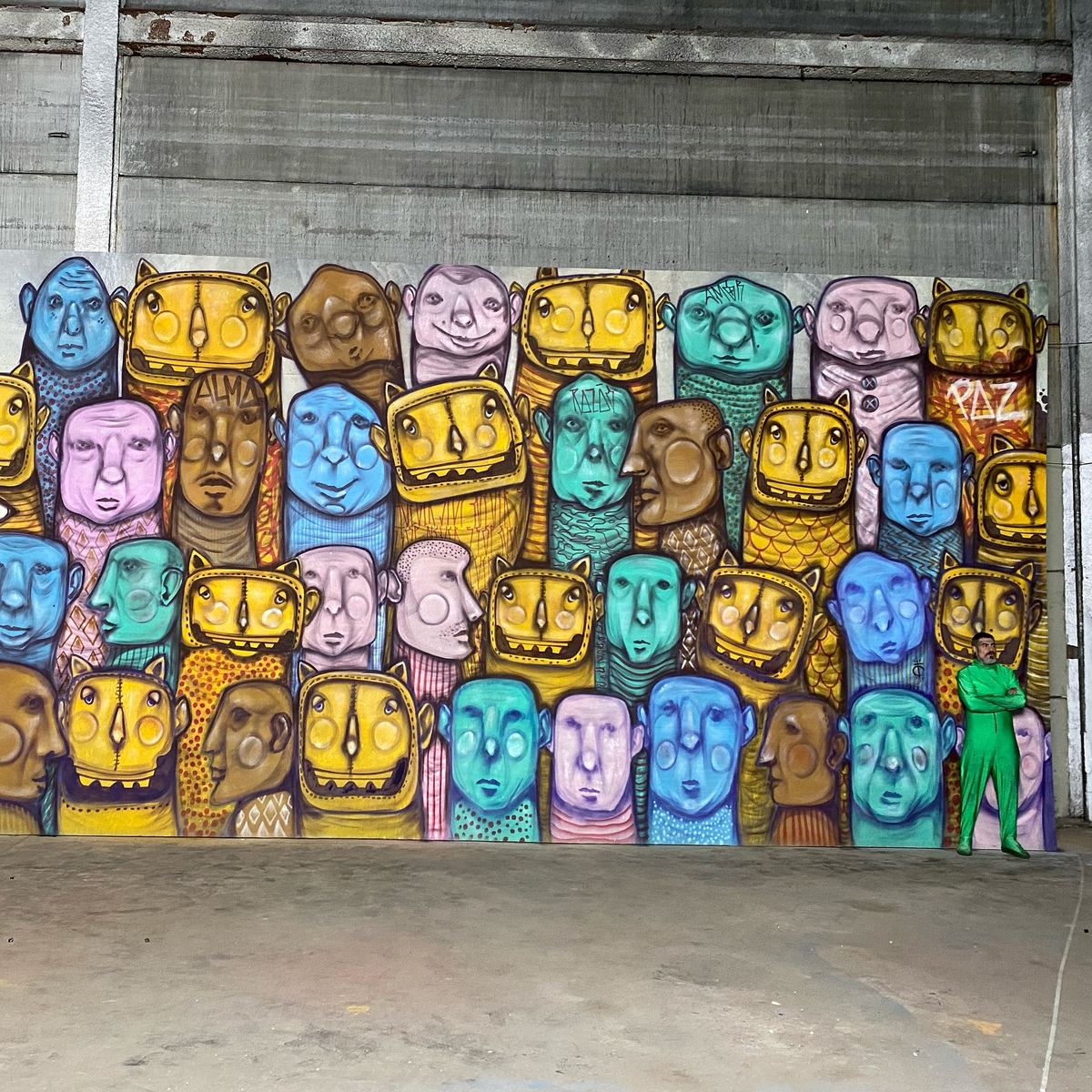 Mural de Tico Canato com dezenas de rostos coloridos ocupando a parede de um galpão