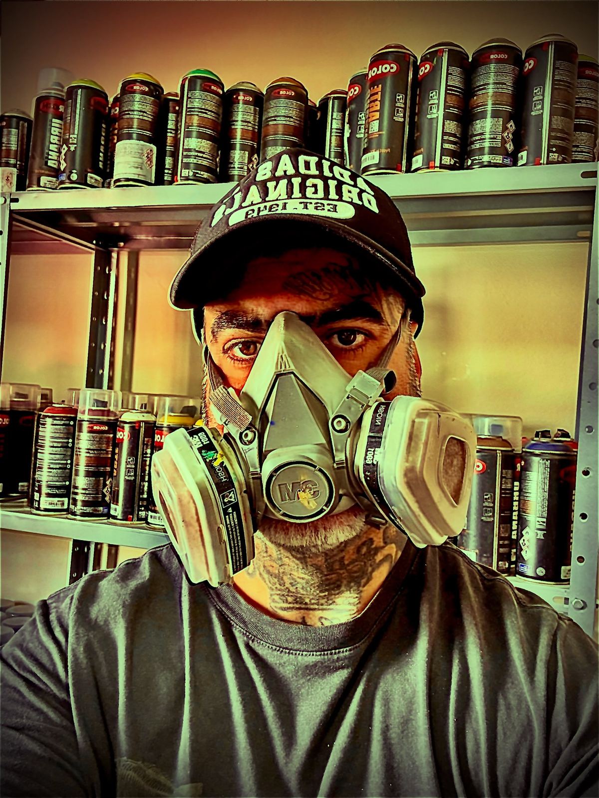 Tico Canato de máscara respiratória diante das prateleiras de latas de spray do ateliê